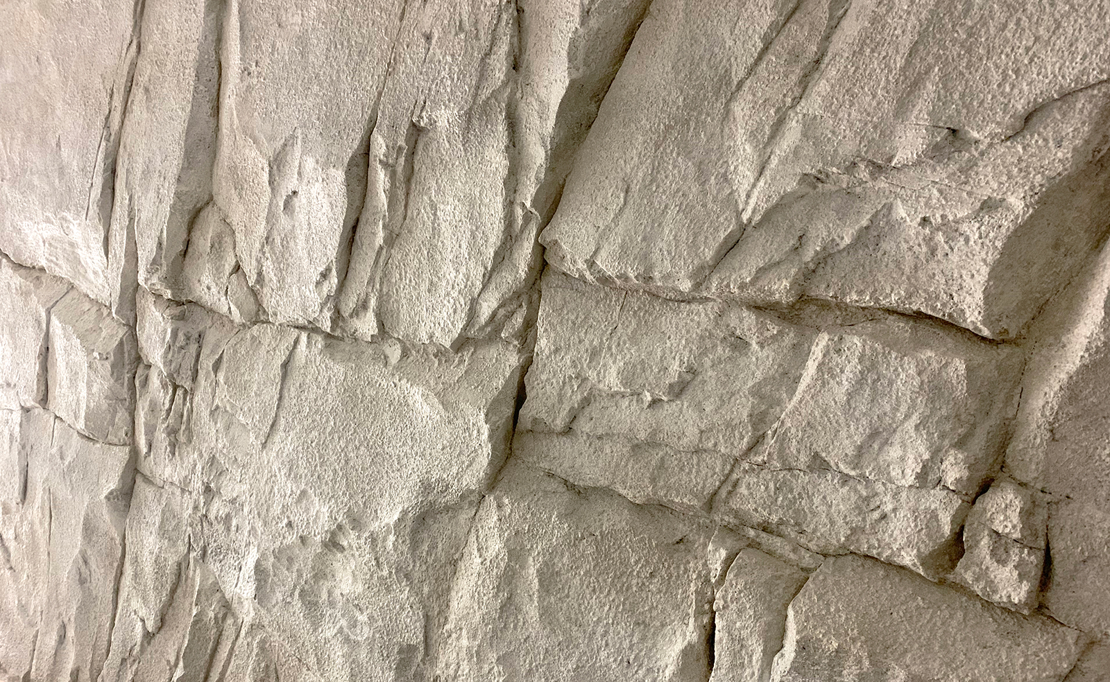 白っぽい、大きな岩を模したモルタル造形で仕上げた壁の写真